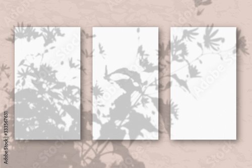 3 vertical sheets of white textured paper on a pastel pink wall background. Mockup with an overlay of plant shadows. Natural light casts a shadow from the top of the field plants and flowers