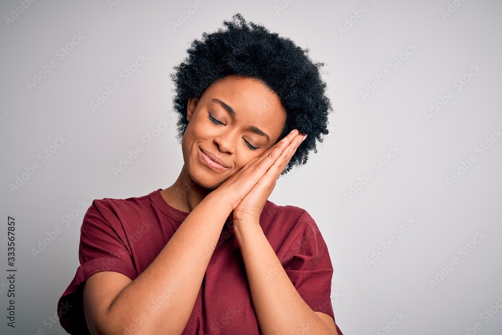 Young beautiful African American afro woman with curly hair wearing casual t-shirt standing sleeping tired dreaming and posing with hands together while smiling with closed eyes. Young beautiful African American afro woman with curly hair wearing casual t-shirt standing sleeping tired dreaming and posing with hands together while smiling with closed eyes.