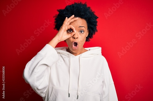 Young beautiful African American afro sportswoman with curly hair wearing sportswear doing ok gesture shocked with surprised face, eye looking through fingers. Unbelieving expression.