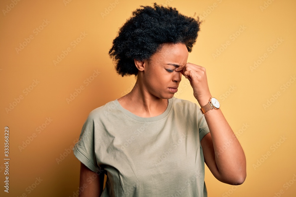 Young beautiful African American afro woman with curly hair wearing casual t-shirt tired rubbing nose and eyes feeling fatigue and headache. Stress and frustration concept. Young beautiful African American afro woman with curly hair wearing casual t-shirt tired rubbing nose and eyes feeling fatigue and headache. Stress and frustration concept.