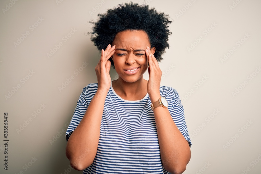 Young beautiful African American afro woman with curly hair wearing striped t-shirt with hand on head for pain in head because stress. Suffering migraine. Young beautiful African American afro woman with curly hair wearing striped t-shirt with hand on head for pain in head because stress. Suffering migraine.