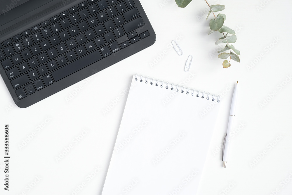 Stylish office table desk. Workspace with laptop keyboard, blank paper notepad, eucalyptus on white background. Flat lay, top view Stylish office table desk. Workspace with laptop keyboard, blank paper notepad, eucalyptus on white background. Flat lay, top view