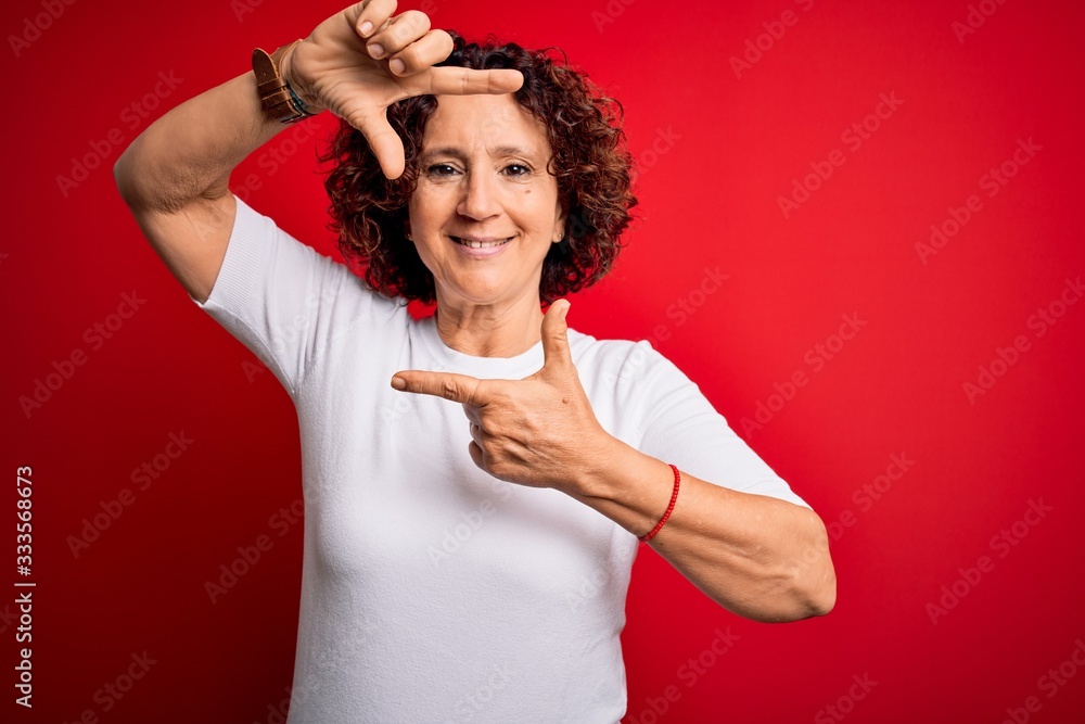 Middle age beautiful curly hair woman wearing casual t-shirt over isolated red background smiling making frame with hands and fingers with happy face. Creativity and photography concept. Middle age beautiful curly hair woman wearing casual t-shirt over isolated red background smiling making frame with hands and fingers with happy face. Creativity and photography concept.