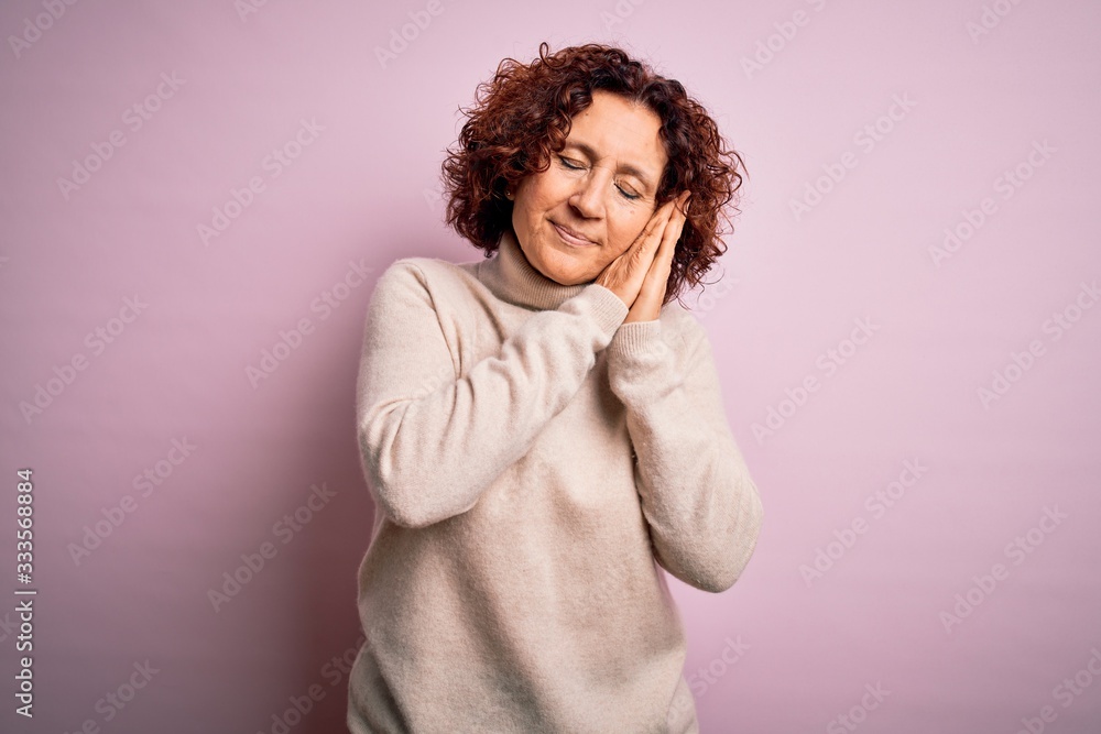 Middle age beautiful curly hair woman wearing casual turtleneck sweater over pink background sleeping tired dreaming and posing with hands together while smiling with closed eyes.