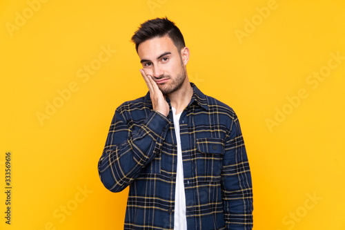 Young handsome man over isolated yellow background unhappy and frustrated