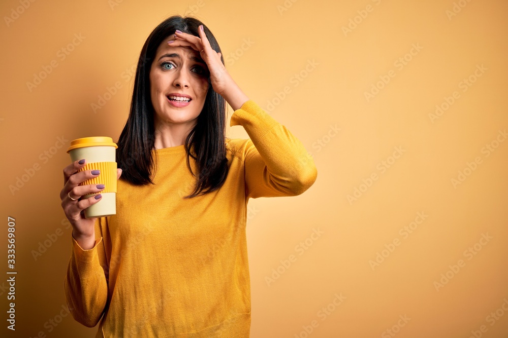 Young woman with blue eyes holding cup of coffee standing over yellow background stressed with hand on head, shocked with shame and surprise face, angry and frustrated. Fear and upset for mistake. Young woman with blue eyes holding cup of coffee standing over yellow background stressed with hand on head, shocked with shame and surprise face, angry and frustrated. Fear and upset for mistake.