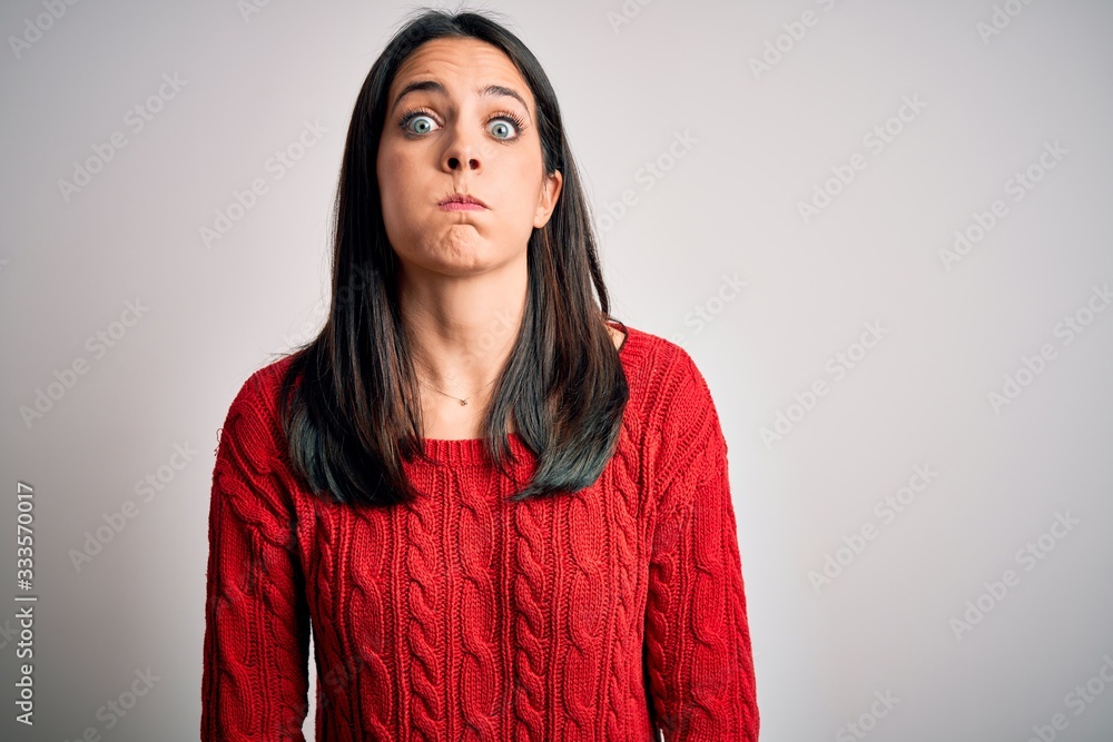 Young brunette woman with blue eyes wearing casual sweater over isolated white background puffing cheeks with funny face. Mouth inflated with air, crazy expression. Young brunette woman with blue eyes wearing casual sweater over isolated white background puffing cheeks with funny face. Mouth inflated with air, crazy expression.