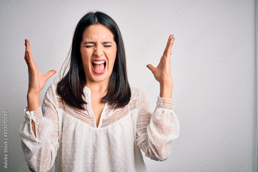 Young brunette woman with blue eyes wearing casual t-shirt over isolated white background celebrating mad and crazy for success with arms raised and closed eyes screaming excited. Winner concept Young brunette woman with blue eyes wearing casual t-shirt over isolated white background celebrating mad and crazy for success with arms raised and closed eyes screaming excited. Winner concept