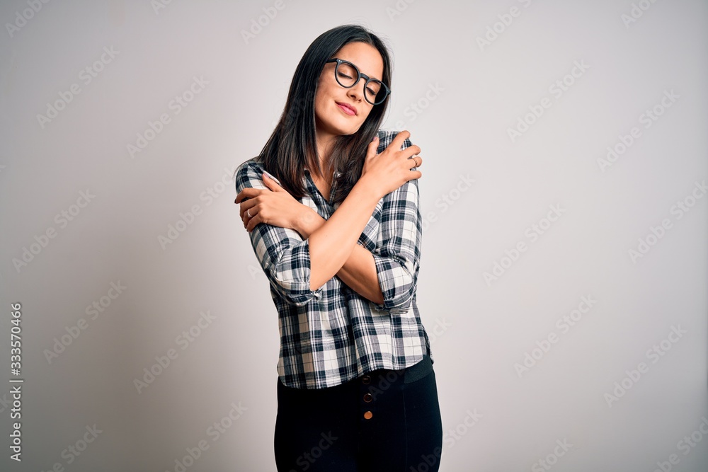 Young brunette woman with blue eyes wearing casual shirt and glasses over white background Hugging oneself happy and positive, smiling confident. Self love and self care Young brunette woman with blue eyes wearing casual shirt and glasses over white background Hugging oneself happy and positive, smiling confident. Self love and self care
