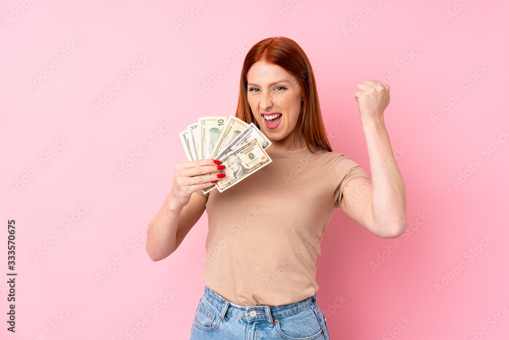 Young redhead woman over isolated pink background taking a lot of money Young redhead woman over isolated pink background taking a lot of money