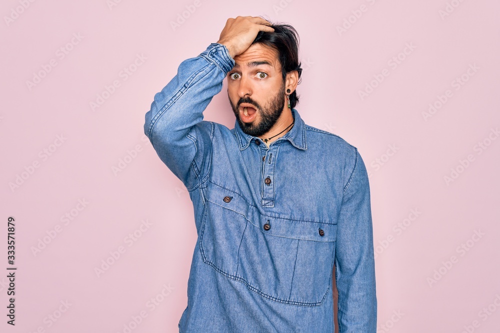 Fototapeta premium Young handsome hispanic bohemian man wearing hippie style over pink background surprised with hand on head for mistake, remember error. Forgot, bad memory concept.
