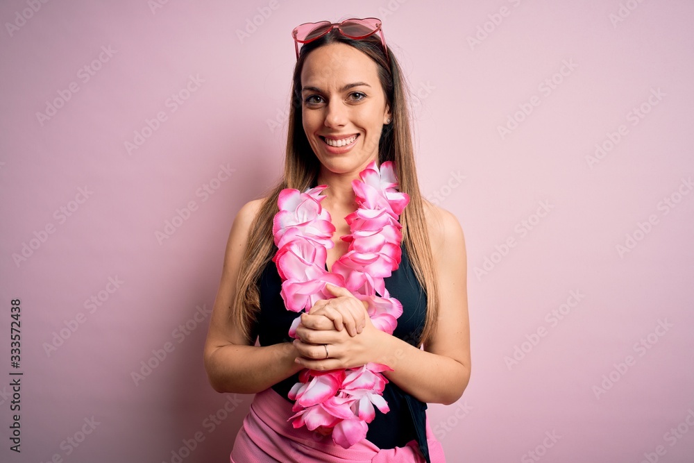 Young beautiful blonde woman wearing swimsuit and floral Hawaiian lei over pink background with hands together and crossed fingers smiling relaxed and cheerful. Success and optimistic Young beautiful blonde woman wearing swimsuit and floral Hawaiian lei over pink background with hands together and crossed fingers smiling relaxed and cheerful. Success and optimistic