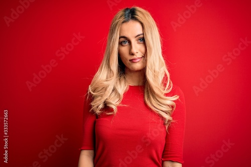 Young beautiful blonde woman wearing casual t-shirt standing over isolated red background looking sleepy and tired, exhausted for fatigue and hangover, lazy eyes in the morning.