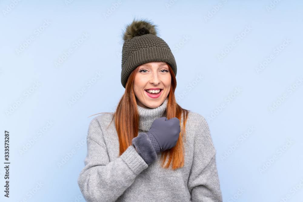 Young redhead Russian woman with winter hat over isolated blue background celebrating a victory Young redhead Russian woman with winter hat over isolated blue background celebrating a victory