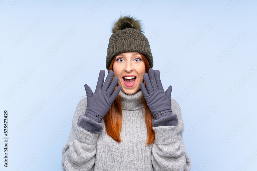 Young redhead Russian woman with winter hat over isolated blue background with surprise facial expression Young redhead Russian woman with winter hat over isolated blue background with surprise facial expression