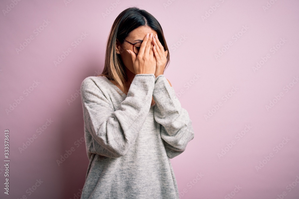 Young beautiful brunette woman wearing casual sweater and glasses over pink background with sad expression covering face with hands while crying. Depression concept. Young beautiful brunette woman wearing casual sweater and glasses over pink background with sad expression covering face with hands while crying. Depression concept.
