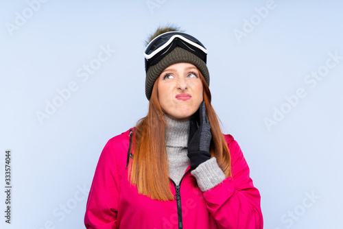 Skier redhead woman with snowboarding glasses over isolated blue wall thinking an idea © luismolinero
