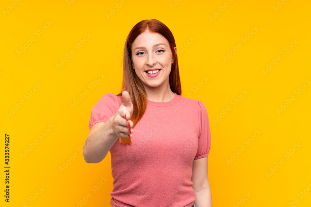 Young redhead woman over isolated yellow background handshaking after good deal Young redhead woman over isolated yellow background handshaking after good deal