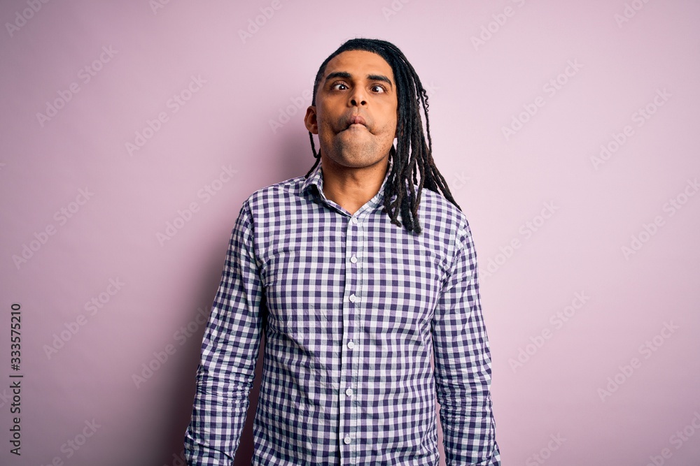Fototapeta premium Young handsome african american afro man with dreadlocks wearing casual shirt making fish face with lips, crazy and comical gesture. Funny expression.