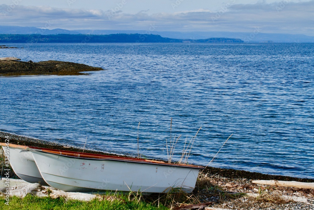 Two white rowboats on the shoreline in a blue bay on Hornby Island, BC. 