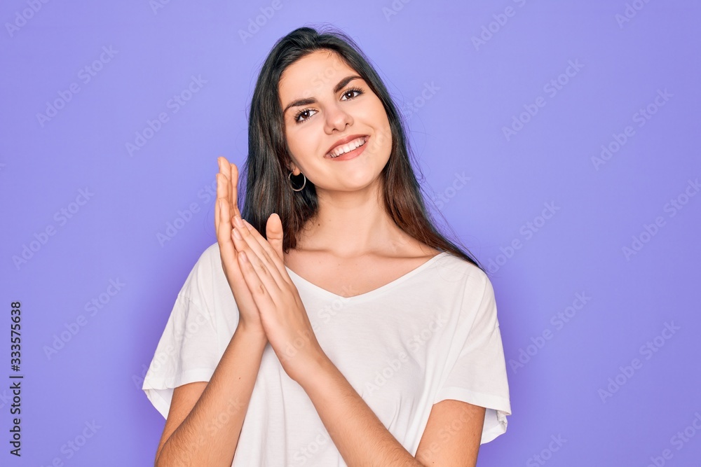Young beautiful brunette woman wearing casual white t-shirt over purple background clapping and applauding happy and joyful, smiling proud hands together Young beautiful brunette woman wearing casual white t-shirt over purple background clapping and applauding happy and joyful, smiling proud hands together