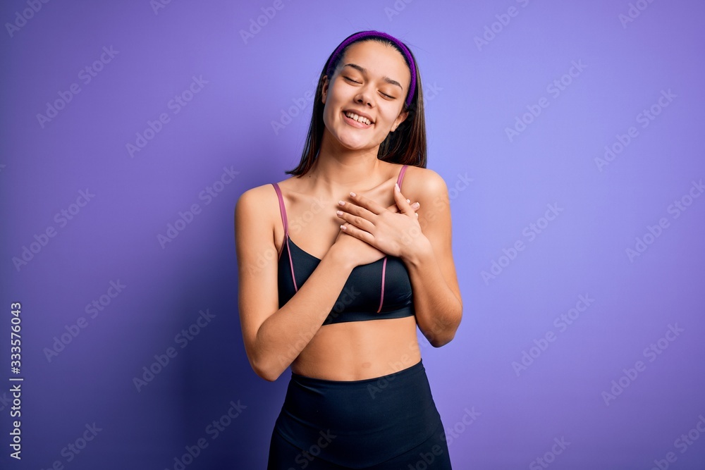 Obraz premium Young beautiful sporty girl doing sport wearing sportswear over isolated purple background smiling with hands on chest with closed eyes and grateful gesture on face. Health concept.