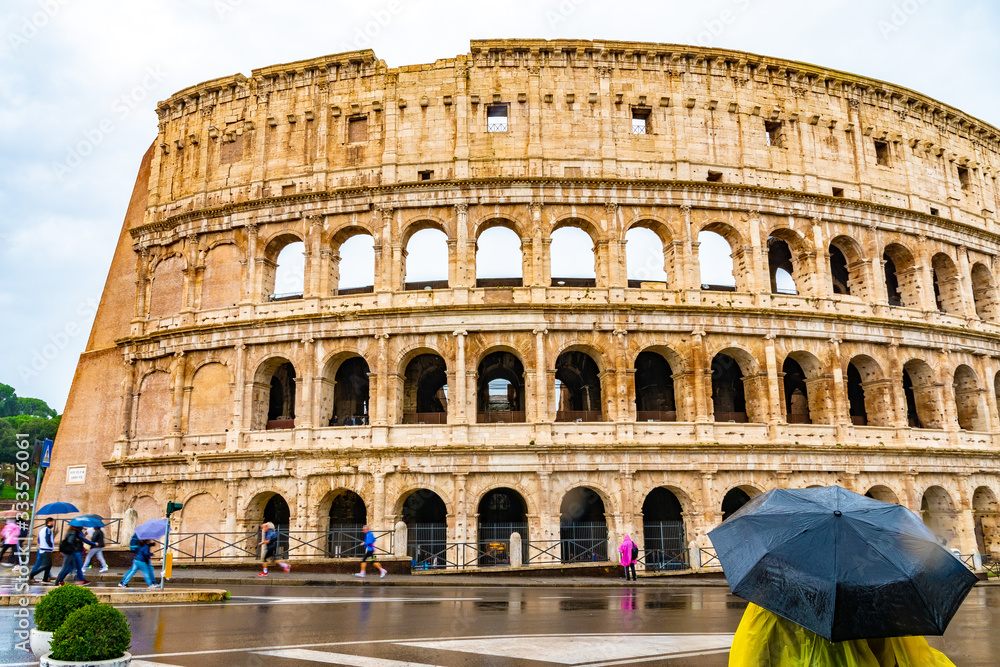 Rome, Italy. Ancient Roman Colosseum, a popular European city amphitheater landmark and tourist attraction with tourists/ people sightseeing. Historic vintage architecture ruins on rainy day.