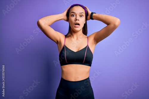 Young beautiful sporty girl doing sport wearing sportswear over isolated purple background Crazy and scared with hands on head, afraid and surprised of shock with open mouth