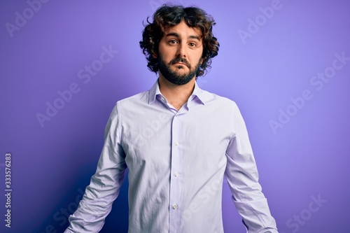 Young handsome business man with beard wearing shirt standing over purple background looking sleepy and tired, exhausted for fatigue and hangover, lazy eyes in the morning. © Krakenimages.com