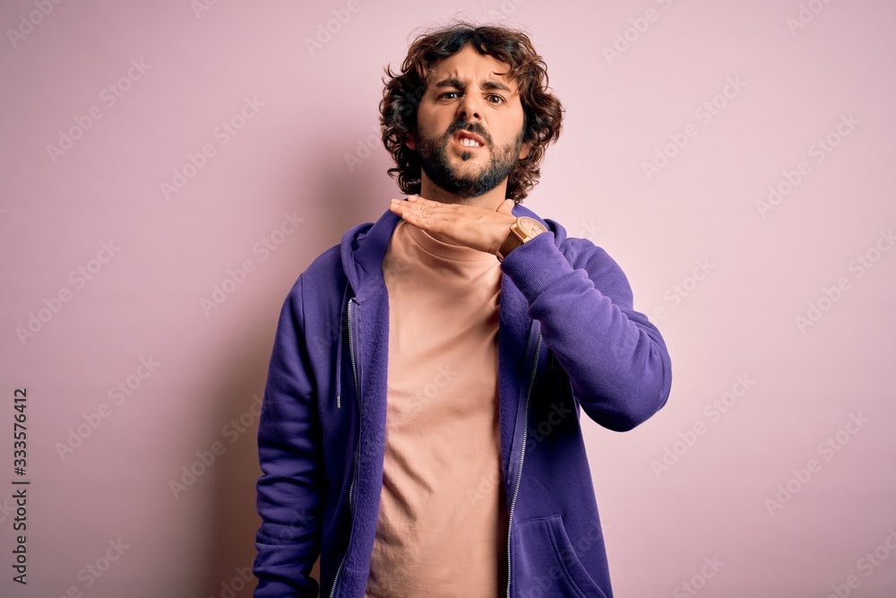 Young handsome sporty man with beard wearing casual sweatshirt over pink background cutting throat with hand as knife, threaten aggression with furious violence Young handsome sporty man with beard wearing casual sweatshirt over pink background cutting throat with hand as knife, threaten aggression with furious violence