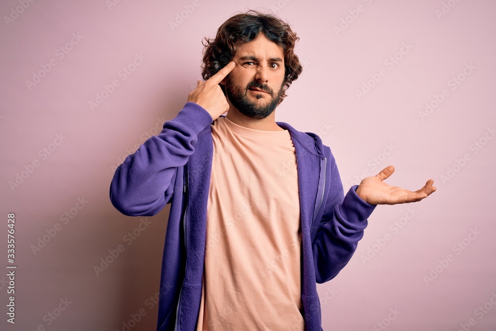 Young handsome sporty man with beard wearing casual sweatshirt over pink background confused and annoyed with open palm showing copy space and pointing finger to forehead. Think about it. Young handsome sporty man with beard wearing casual sweatshirt over pink background confused and annoyed with open palm showing copy space and pointing finger to forehead. Think about it.