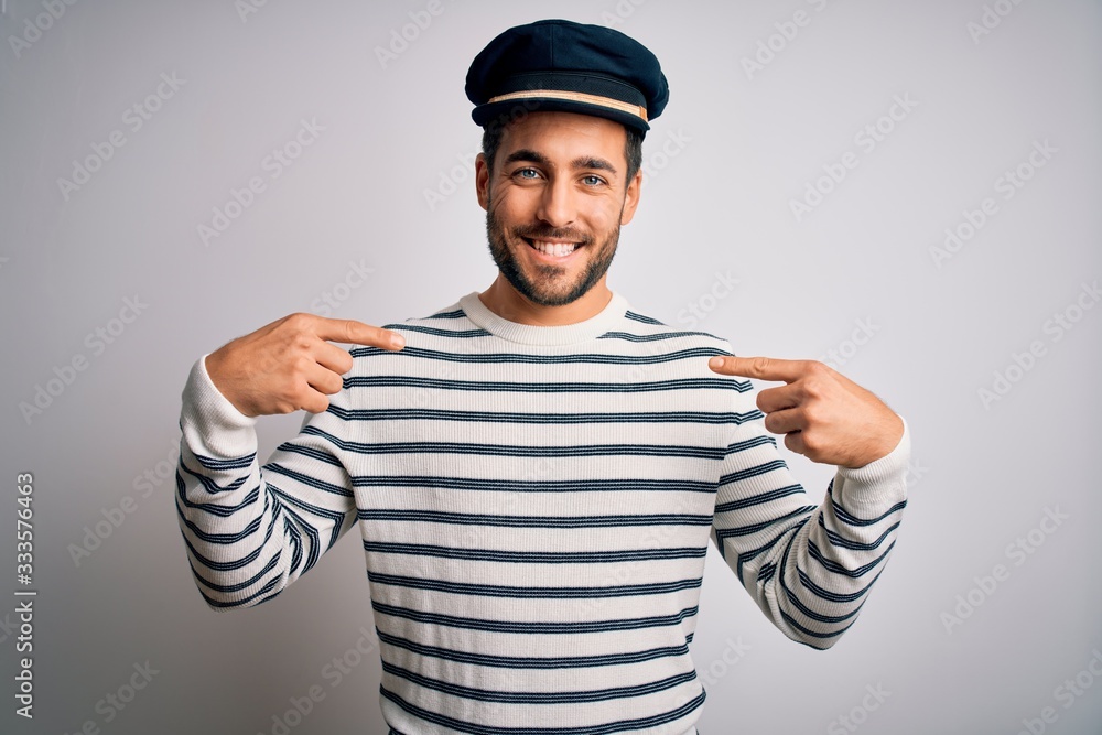 Young handsome sailor man with beard wearing navy striped uniform and captain hat looking confident with smile on face, pointing oneself with fingers proud and happy. Young handsome sailor man with beard wearing navy striped uniform and captain hat looking confident with smile on face, pointing oneself with fingers proud and happy.