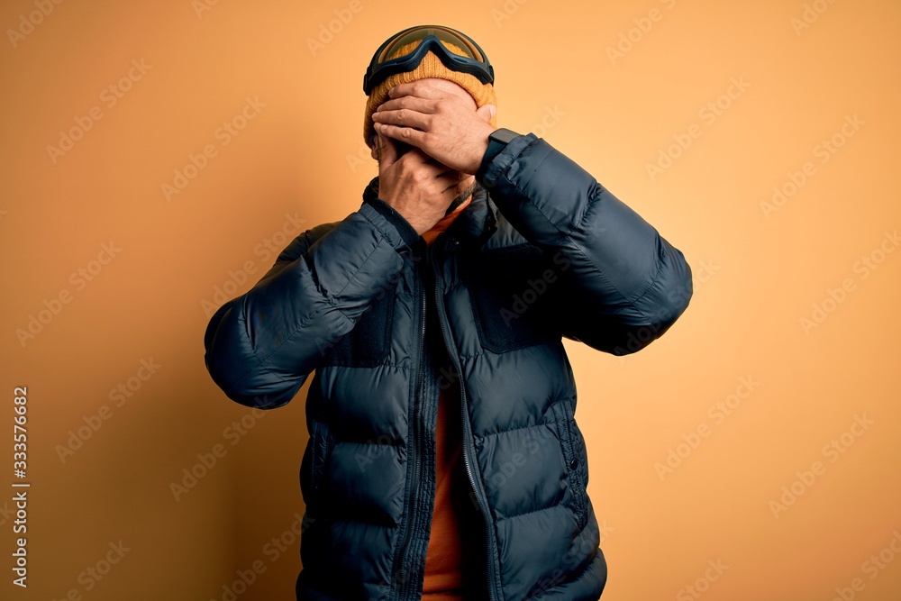 Young handsome skier man with beard wearing snow sportswear and ski goggles Covering eyes and mouth with hands, surprised and shocked. Hiding emotion Young handsome skier man with beard wearing snow sportswear and ski goggles Covering eyes and mouth with hands, surprised and shocked. Hiding emotion
