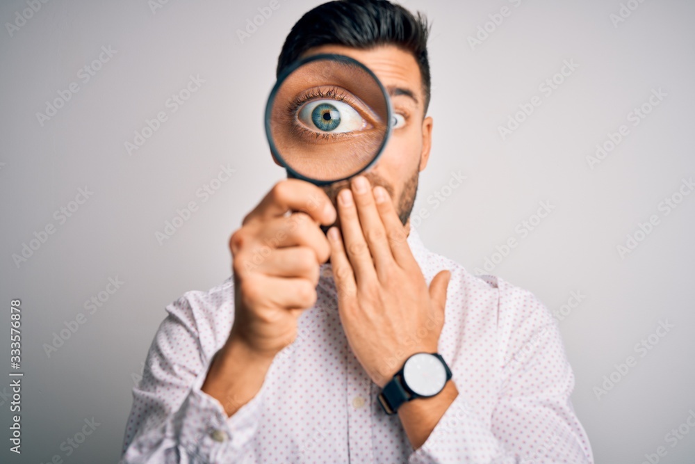 Young detective man looking through magnifying glass over isolated background cover mouth with hand shocked with shame for mistake, expression of fear, scared in silence, secret concept Young detective man looking through magnifying glass over isolated background cover mouth with hand shocked with shame for mistake, expression of fear, scared in silence, secret concept