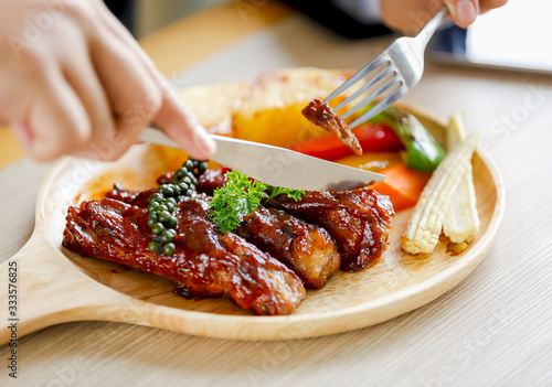 Grilled meat with vegetables on white plate, eating with fork and knife on table in restaurant