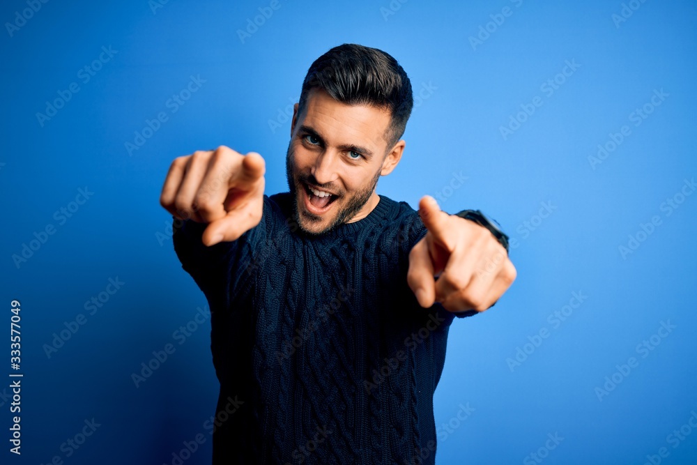 Fototapeta premium Young handsome man wearing casual sweater standing over isolated blue background pointing to you and the camera with fingers, smiling positive and cheerful
