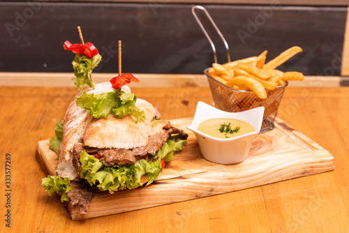 meat sandwich with fries over a wooden table photo