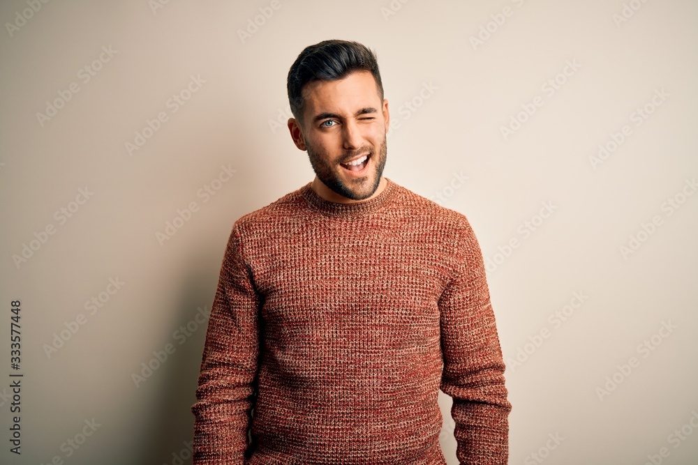 Young handsome man wearing casual sweater standing over isolated white background winking looking at the camera with sexy expression, cheerful and happy face. Young handsome man wearing casual sweater standing over isolated white background winking looking at the camera with sexy expression, cheerful and happy face.