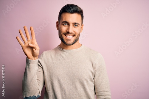 Young handsome man wearing casual sweater standing over isolated pink background showing and pointing up with fingers number four while smiling confident and happy.