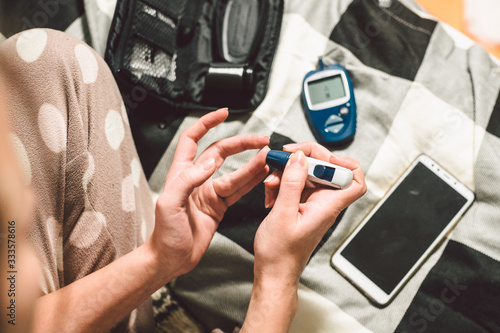 Theme diabetes. A close-up macro plan. Hands of a young Caucasian woman at home in the bedroom on the bed. It uses the technology of an instrument for measuring the level of glucose in the blood photo