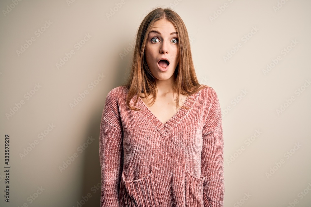 Young beautiful redhead woman wearing pink casual sweater over isolated white background afraid and shocked with surprise and amazed expression, fear and excited face. Young beautiful redhead woman wearing pink casual sweater over isolated white background afraid and shocked with surprise and amazed expression, fear and excited face.