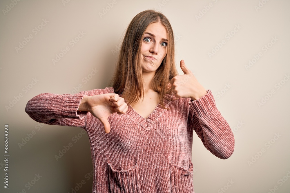 Young beautiful redhead woman wearing pink casual sweater over isolated white background Doing thumbs up and down, disagreement and agreement expression. Crazy conflict Young beautiful redhead woman wearing pink casual sweater over isolated white background Doing thumbs up and down, disagreement and agreement expression. Crazy conflict