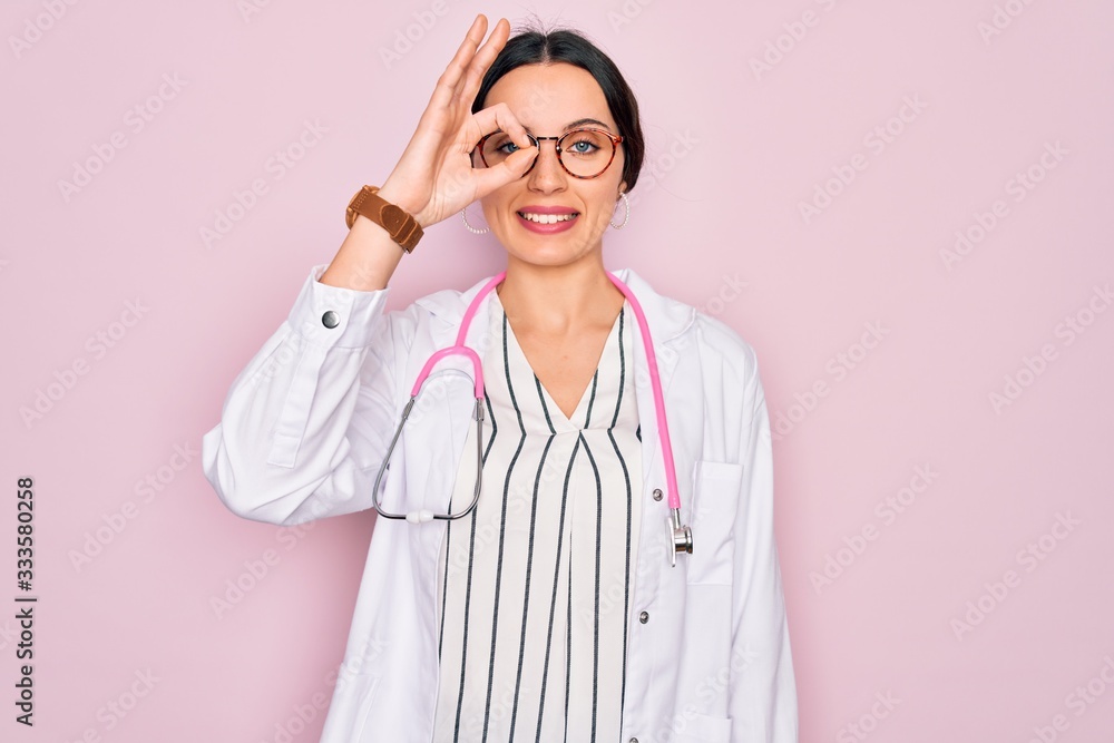 Beautiful doctor woman with blue eyes wearing coat and stethoscope over pink background doing ok gesture with hand smiling, eye looking through fingers with happy face. Beautiful doctor woman with blue eyes wearing coat and stethoscope over pink background doing ok gesture with hand smiling, eye looking through fingers with happy face.