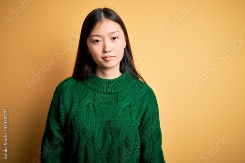 Young beautiful asian woman wearing green winter sweater over yellow isolated background looking sleepy and tired, exhausted for fatigue and hangover, lazy eyes in the morning. © Krakenimages.com