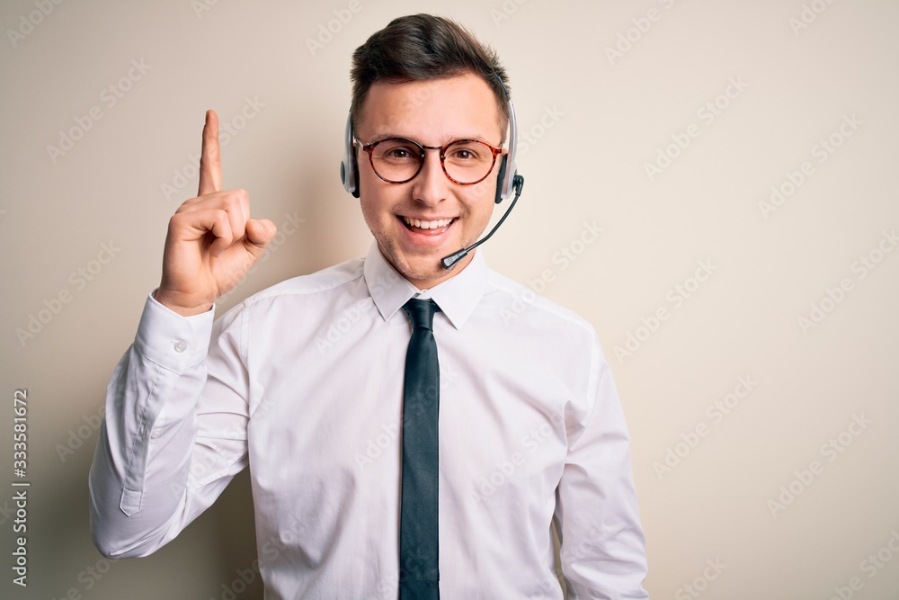 Young handsome caucasian business man wearing call center headset at customer service pointing finger up with successful idea. Exited and happy. Number one. Young handsome caucasian business man wearing call center headset at customer service pointing finger up with successful idea. Exited and happy. Number one.