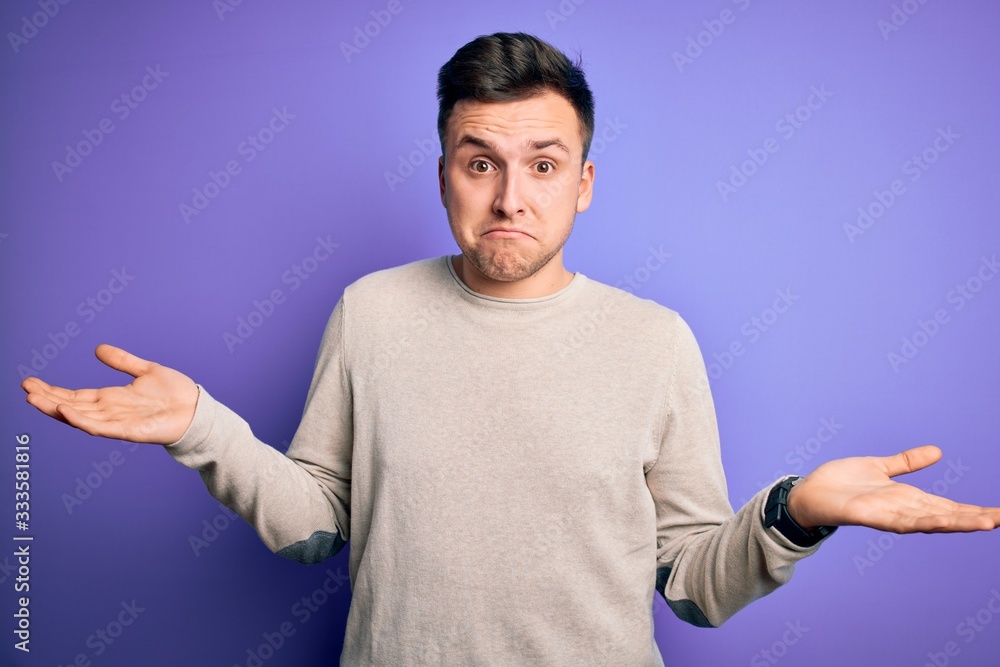 Young handsome caucasian man wearing casual sweater over purple isolated background clueless and confused expression with arms and hands raised. Doubt concept. Young handsome caucasian man wearing casual sweater over purple isolated background clueless and confused expression with arms and hands raised. Doubt concept.