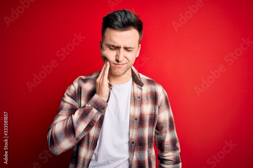 Young handsome caucasian man wearing casual modern shirt over red isolated background touching mouth with hand with painful expression because of toothache or dental illness on teeth. Dentist
