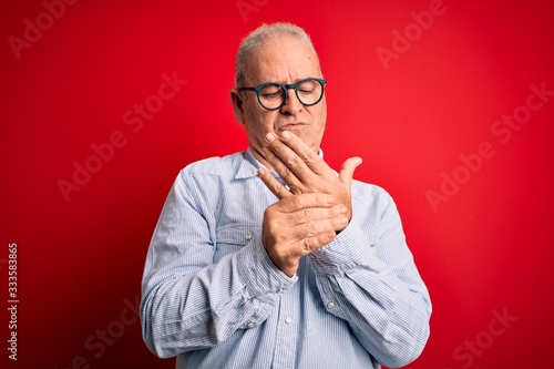 Middle age handsome hoary man wearing casual striped shirt and glasses over red background Suffering pain on hands and fingers, arthritis inflammation © Krakenimages.com