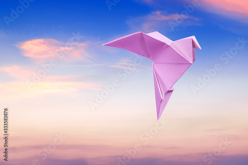 Pink Dove In The Sky At Sunrise. Paper dove of peace on a blue sky background.