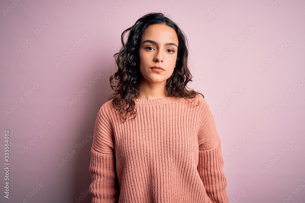 Young beautiful woman with curly hair wearing casual sweater over isolated pink background Relaxed with serious expression on face. Simple and natural looking at the camera. Young beautiful woman with curly hair wearing casual sweater over isolated pink background Relaxed with serious expression on face. Simple and natural looking at the camera.